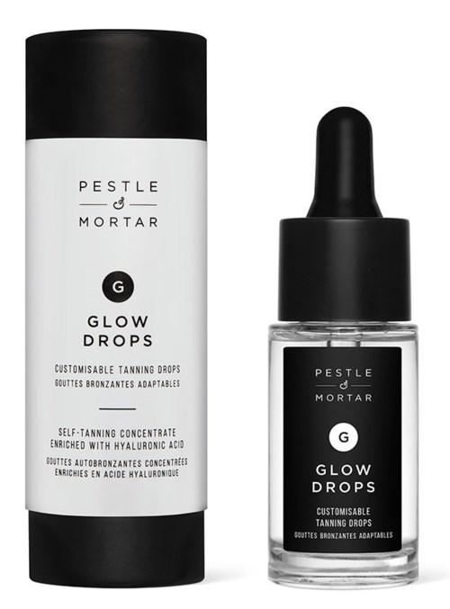 Een zwart-witte fles en doos van PESTLE & MORTAR Glow Drops, een zelfbruiningsproduct met hyaluronzuur.
