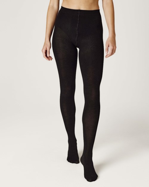 A woman wears black tights that fit tightly and reach her waist, covering her legs completely.