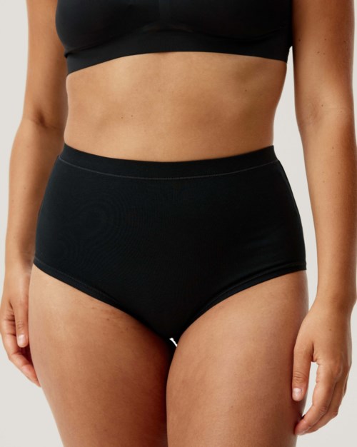Eine Frau trägt schwarze High-Waist-Unterwäsche und ein schwarzes Crop-Top, das ihren Bauch und Teil ihrer Hüften zeigt.