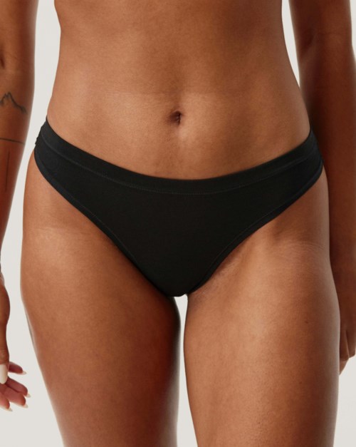 Eine Frau trägt schwarze Unterwäsche, zeigt ihre Taille und oberen Oberschenkel.