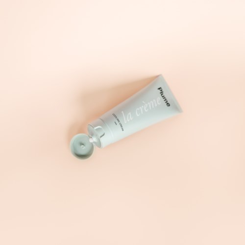 Eine weiße Creme-Tube mit einer kleinen Menge herausgedrückt liegt auf einem rosa Hintergrund.
