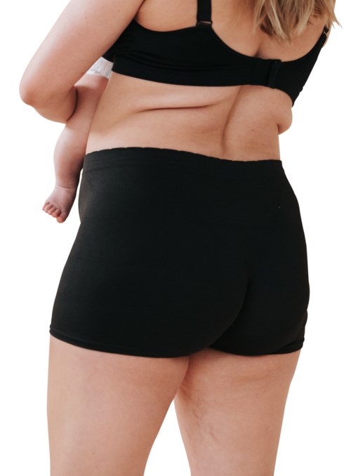 Eine Frau in schwarzen Shorts und Oberteil trägt ein Baby auf dem Rücken.