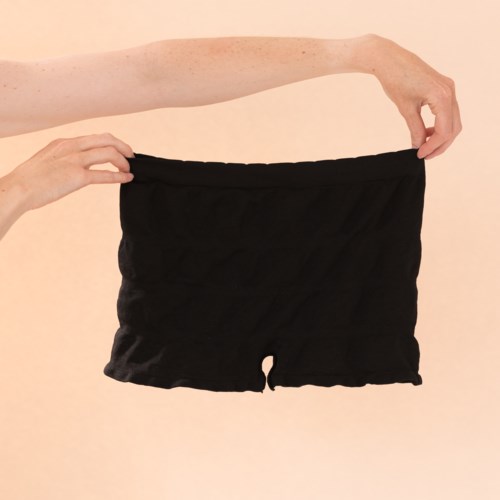 Eine Person hält schwarze Shorts vor einem hellen Hintergrund.