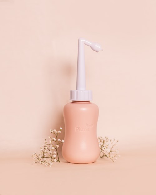 Eine rosa Wasserflöte mit weißer Düse, umgeben von kleinen weißen Blumen auf beige Hintergrund.