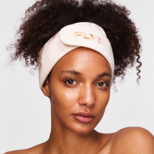 Een vrouw met krullend haar draagt een crèmekleurige hoofdband met oranje tekst en kijkt recht in de camera.