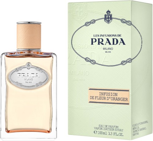Een parfumfles en doos in lichtgroen met blauw logo en tekst over Prada en oranjebloesemsgeur.