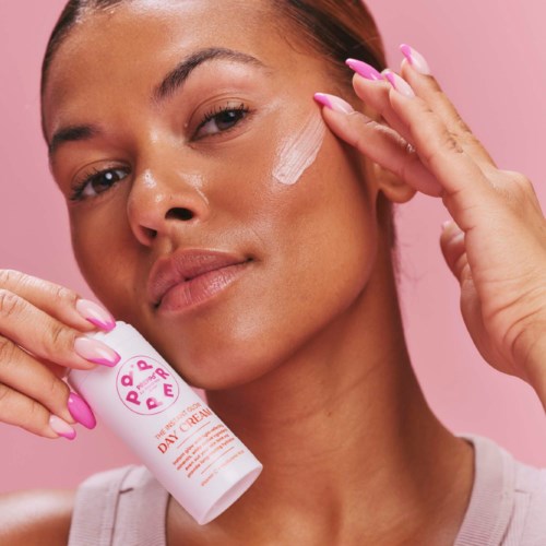 A woman applies cream to her face, holding a bottle labeled 'Day Cream' in her hand.