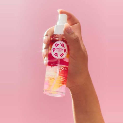 A hand holds a pink spray bottle with a pink label against a pink background.