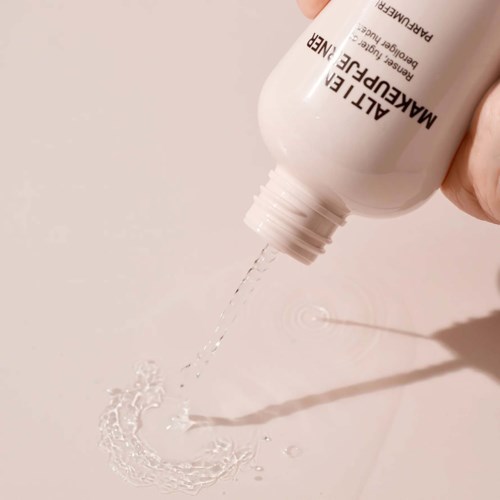 Eine weiße Flasche mit der Aufschrift ALITTLE MAKEUP REMOVER gießt klare Flüssigkeit auf eine Oberfläche.