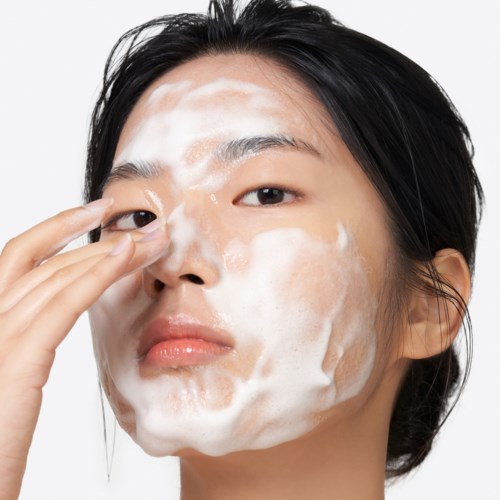 A woman washes her face with a foamy substance, looking serious and focused.