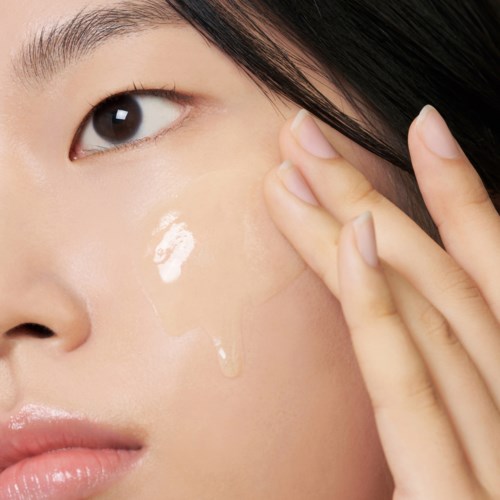 A woman applies a clear skincare gel to her cheek, showing smooth skin and black hair.