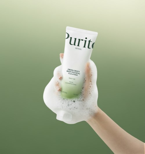 Een hand vasthoudt een groene en witte tube van Purito huidverzorgingsproduct met schuim.