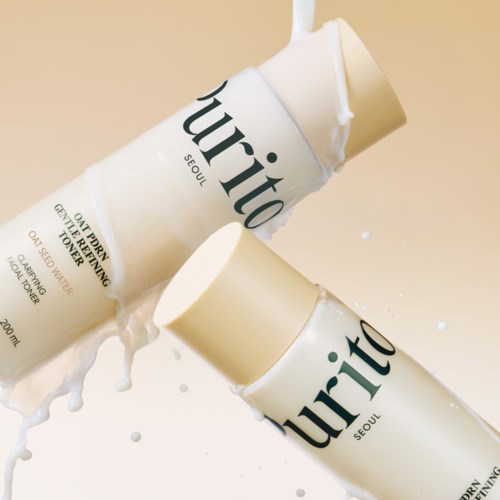 To flasker med hudpleieproduktet Purito ligger på en overflate, med noen væske sølt rundt dem.