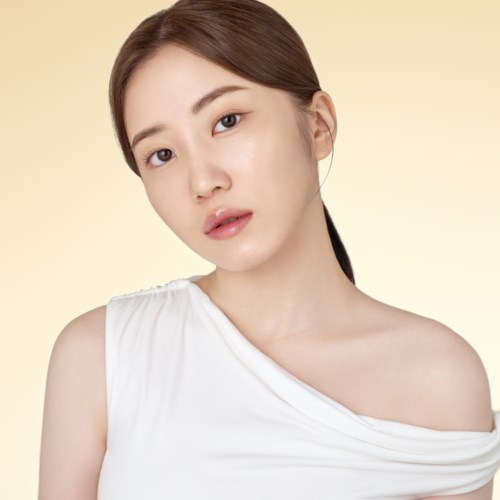 Eine junge Frau mit heller Haut und braunen Haaren in einem weißen Off-Shoulder-Top vor einem hellgelben Hintergrund.