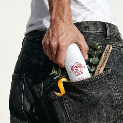A man puts deodorant in his back pocket along with a small tool and some leaves.