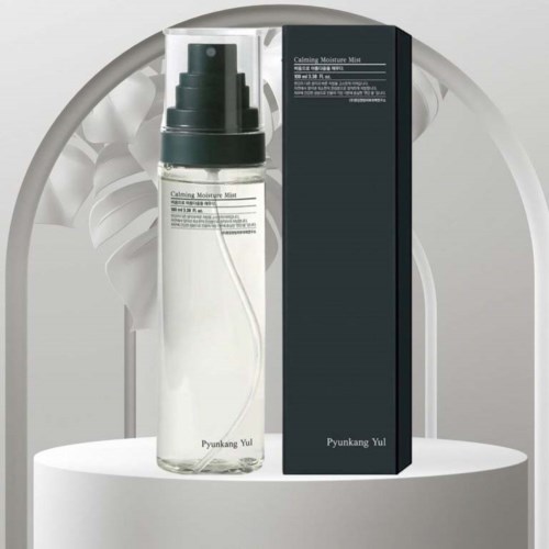 A bottle of calming moisture mist and its box with simple design, placed on a round white surface.