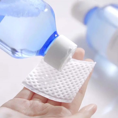 Eine Hand hält einen Wattepad, neben einer Flasche Flüssigkeit, wahrscheinlich für Reinigung oder Hautpflege.