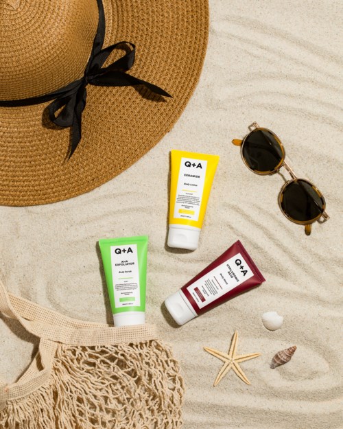 Ein Sonnenhut, Sonnenbrille, Lotion-Tuben, weiße Ball, Seestern, Muschel und Netzbeutel am Strand.