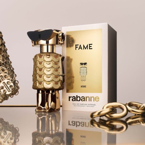Ein Parfümflasche mit Gold- und Glitzergestaltung, neben einer Schachtel mit 'FAME' von Rabanne und Goldketten.