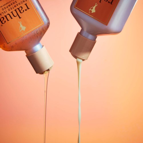 Two bottles tipped upside down with lotion or soap pouring out against an orange background.