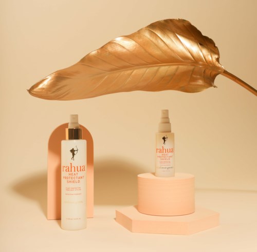 Two skincare bottles are displayed on pink blocks, with a large golden leaf overhead, creating a stylish, minimal setup.