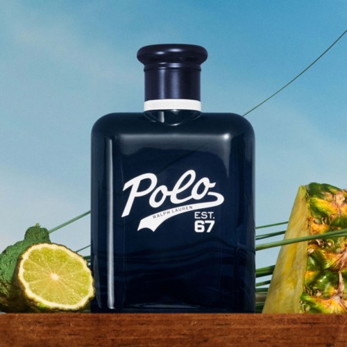 Een donkerblauwe Polo Ralph Lauren fles met witte tekst, omgeven door limoen, ananas en groen op een houten oppervlak.