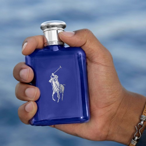 Een hand die een blauwe fles vasthoudt met een wit logo van een paard en ruiter, voor water op de achtergrond.