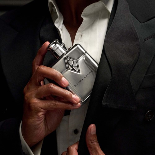 Persoon in pak houdt een Ralph Lauren parfumfles tegen de borst.