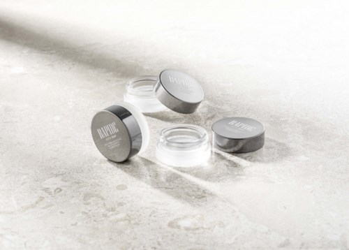 Drie kleine containers met labels liggen op een lichte ondergrond, sommige deksels zijn eraf, tonen lege inhoud. Zwart en wit.