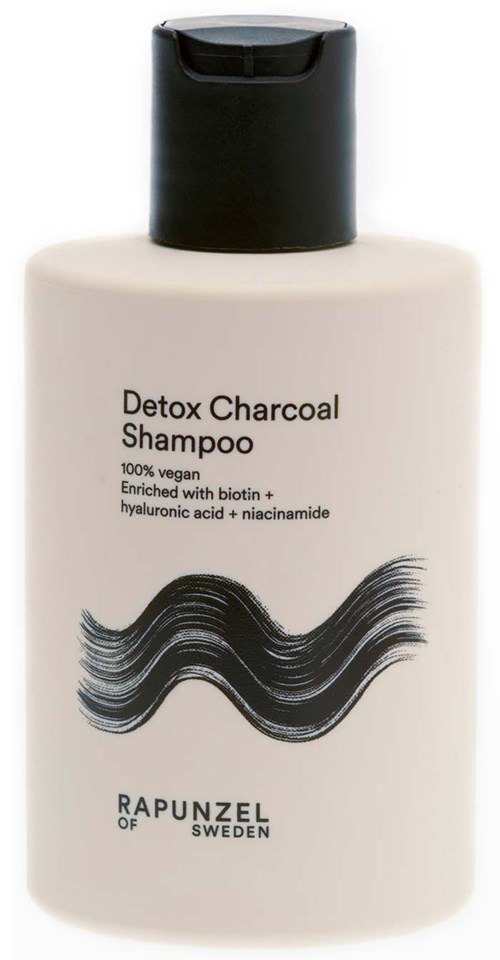 En hvit flaske med Detox Charcoal Shampoo med svart lokk, med bølgende svarte linjer og tekstdetaljer.