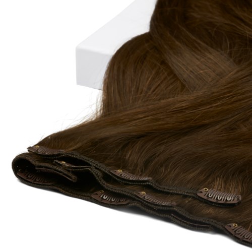 Een close-up van een bruin haarstuk met zwart gaas en fijne haarlijntjes op een witte ondergrond.