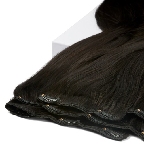 Bundles of dark hair extensions with clips and a bun, placed on a white surface.