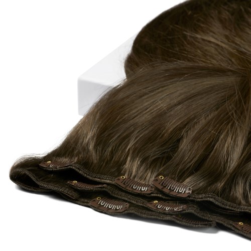 En brun peruk med lace front, placerad på en vit yta.