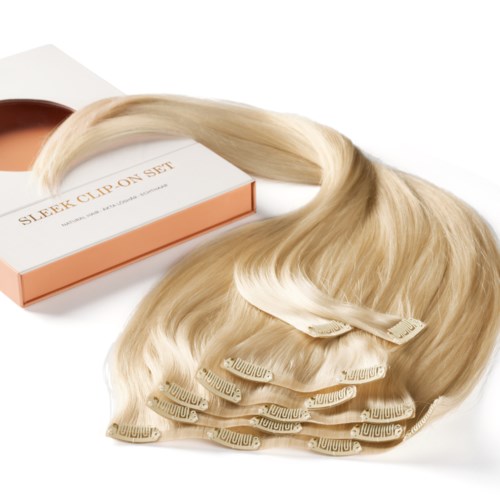 En set med ljusblont hårförlängning med clips, bredvid en rosa och vit låda märkt "Sleek Clip On Set."