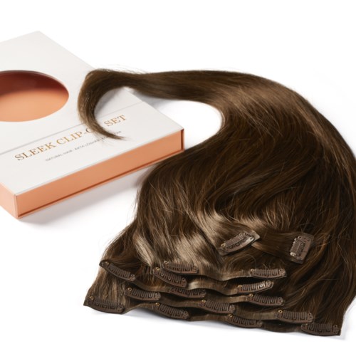 Ett set bruna hårförlängningar med clips, placerade bredvid en vit och rosa box märkt 'Sleek Clip Set.'
