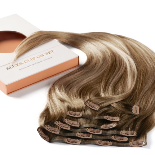 Ein Satz Haarverlängerungen oder Haarteile mit Clips in Blond, neben einer Box angeordnet. Die Box trägt die Aufschrift "Sleek Clip-On Set."