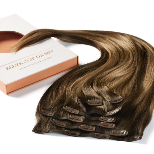 Ein Satz braune Haarverlängerungen mit Clips, neben einer weißen und rosafarbenen Schachtel.