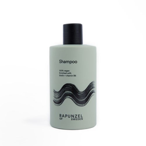 Vähän vihreä shampoo-pullo, musta korkki, merkki ja kuvaus, musta aaltoileva viivamainen muoto.