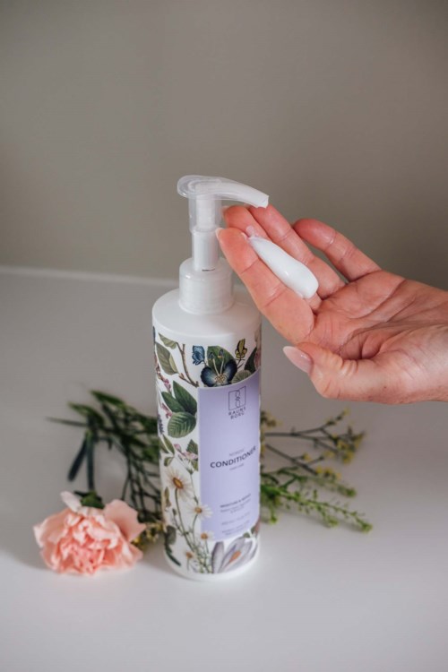 Jemand drückt Handdesinfektionsmittel aus einer Blumenkokonflasche auf die Hand. Auf dem Tisch liegen Blumen.