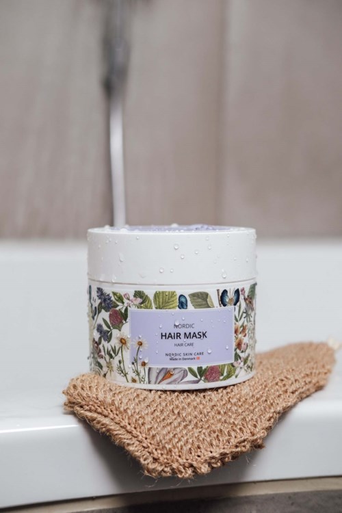 A container of Nordic hair mask on a brown cloth, placed on a white surface with a sink in the background.