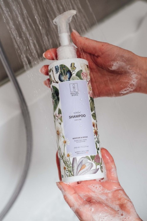 Jemand hält eine Shampoo-Flasche unter fließendes Wasser im Badezimmer.