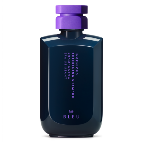 Eine dunkelblaue Flasche mit lila Deckel enthält Shampoo mit der Aufschrift 'R+CO Bleu Ignitious Thickening Shampoo' in lila Text.