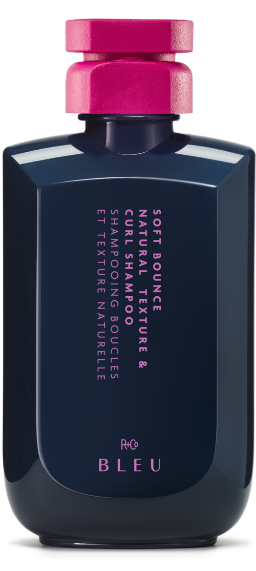 A dark blue bottle with a pink cap, labeled with white and pink text about scent and ingredients.