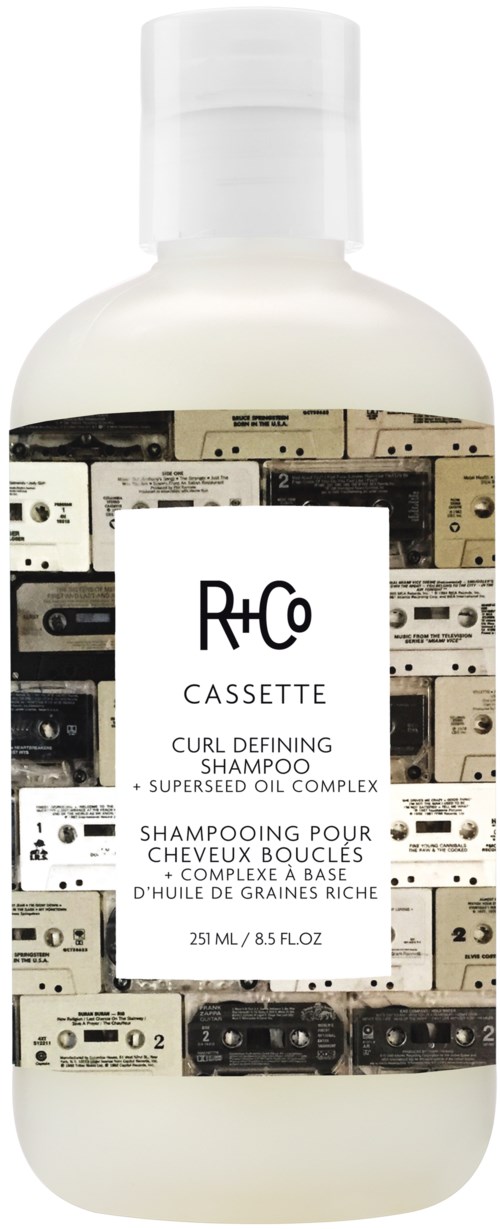 En hvit flaske med R+Co Cassette-sjampo med etikett som viser kassettbånd og tekst.