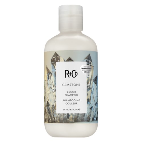 Een witte fles met een label met kristalafbeeldingen, gemarkeerd R+Co Gemstone kleurshampoo, 241ml.
