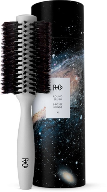 Eine runde Haarbürste mit weißem Griff und schwarzen Borsten sowie eine himmelartige Verpackung im Hintergrund.