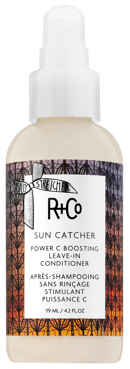 En hvit sprayflaske merket R+Co Sun Catcher med oransje og svart design, inneholder leave-in balsam med vitamin C.