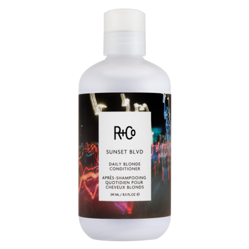 Een witte fles met zwart label toont R+Co Sunset Blvd conditioner voor blond haar, met kleurrijk stadslichtenillustratie.