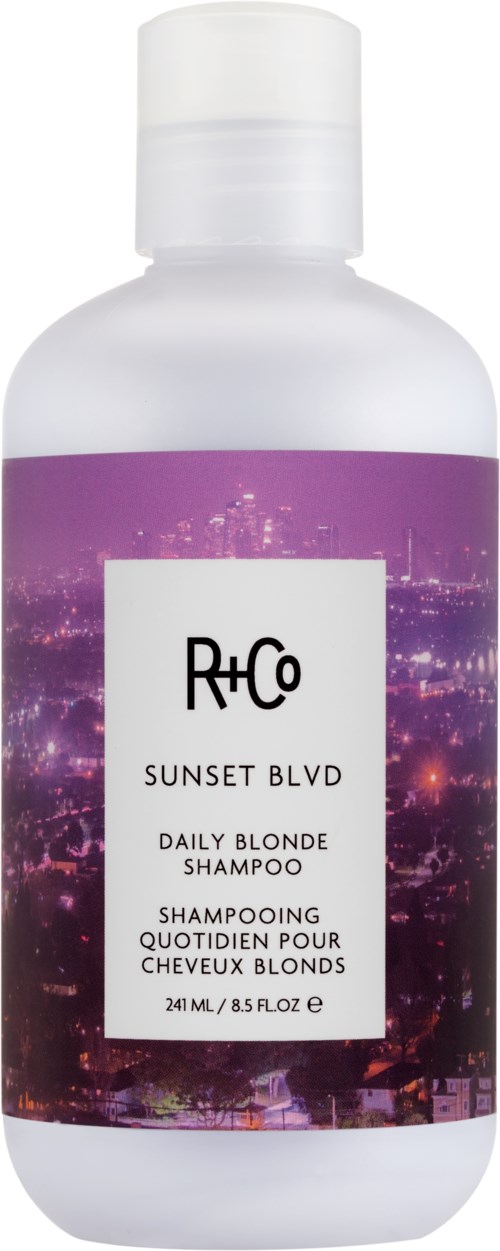 A white shampoo bottle labeled R+Co Sunset Blvd Daily Blonde Shampoo with a cityscape background design.