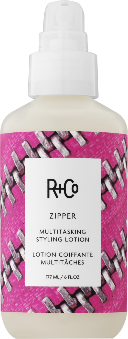 Valkoinen suihkepullo, jossa pinkki etiketti ja vetoketju kuvio ja teksti 'R+Co Zipper Multitasking Styling Lotion.'